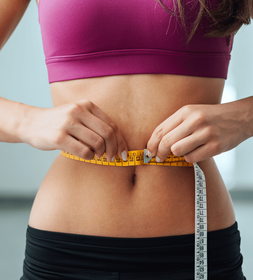 A person measuring their waist with a yellow tape measure, wearing a pink sports bra and black workout pants.