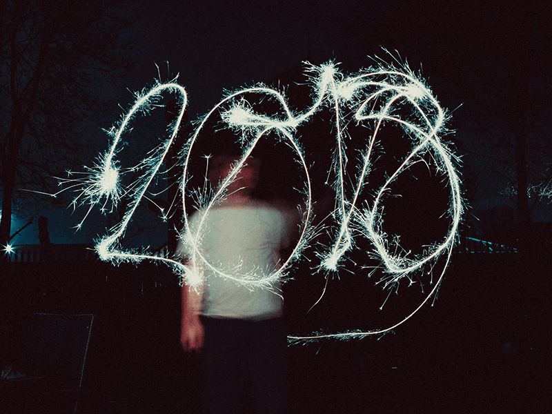 A person creates the numbers "2018" in the air using a sparkler against a dark background, as if painting a vivid 2018 Review with light.