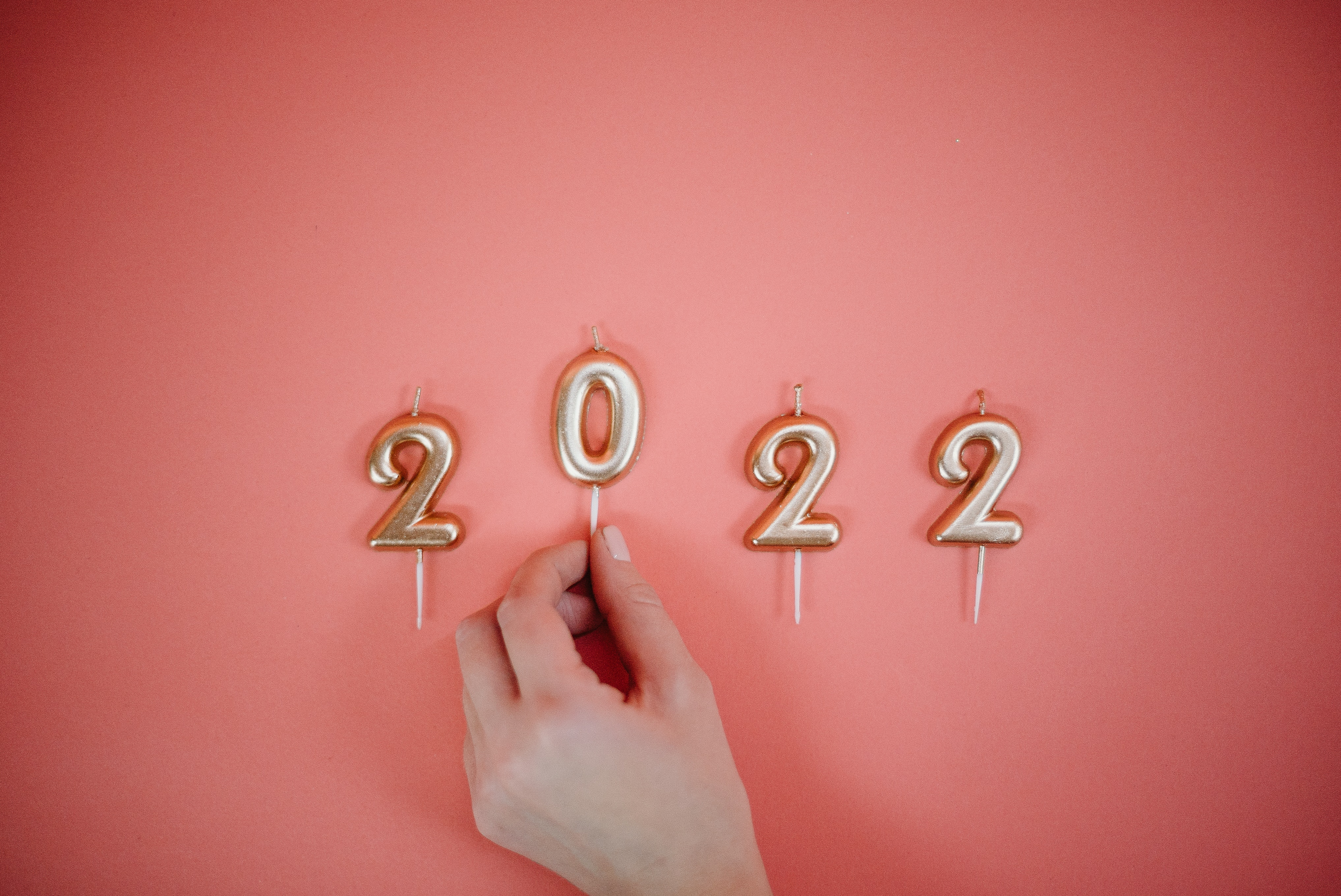 A hand arranges golden number candles forming "2022" on a red background.