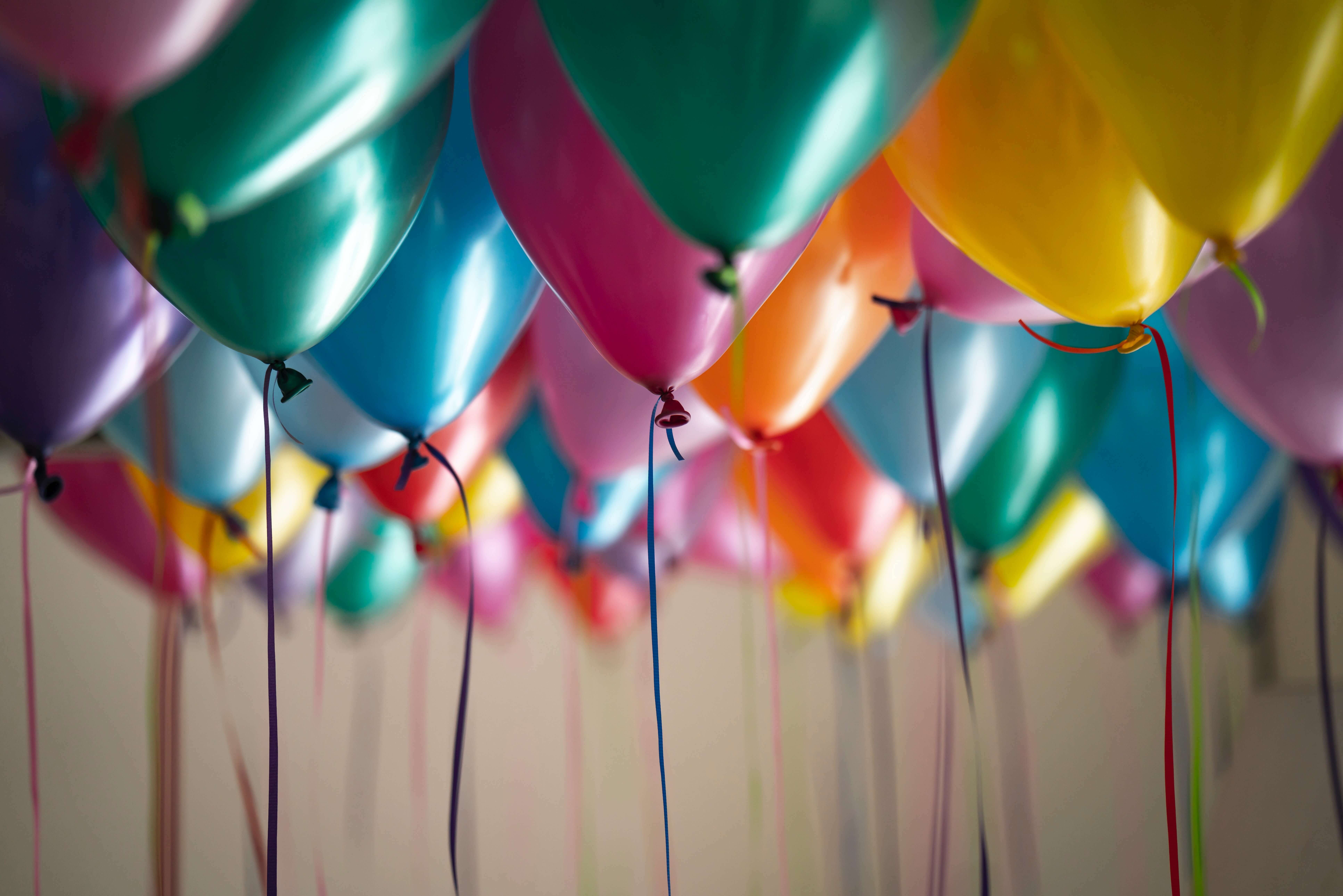 A close-up of numerous colorful balloons, including green, pink, orange, blue, and yellow, floating tied with strings.