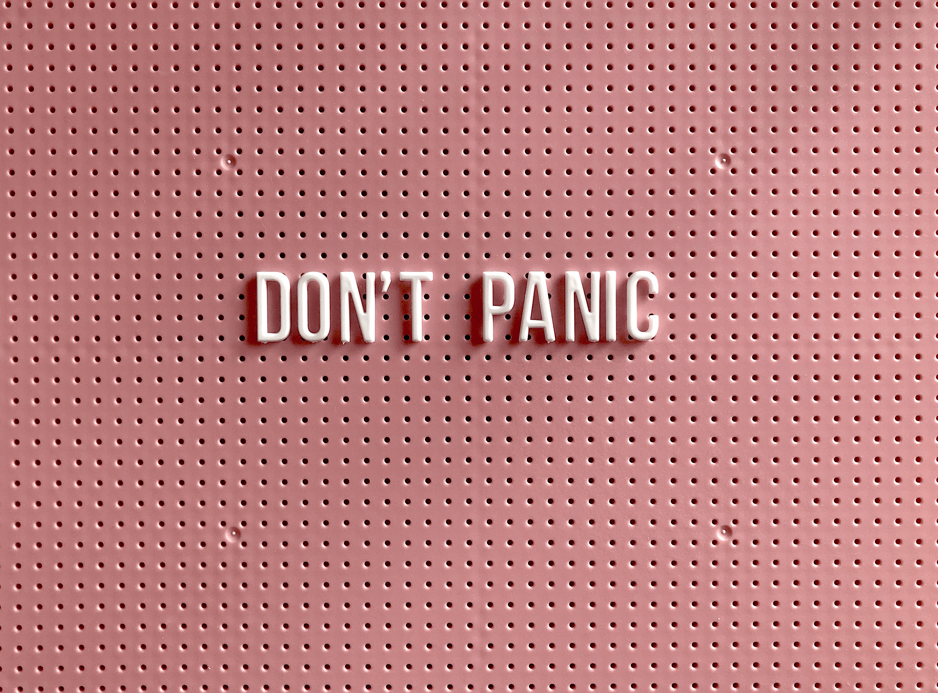 A pink pegboard with the words "DON'T PANIC" displayed in white letters.