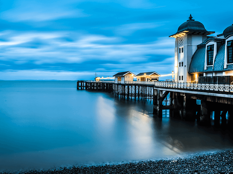 A long exposure photo of a pier extending into a calm sea with a building featuring domed roofs captures the serene essence of ten lessons I’ve learned from ten years in business (Part 1 of 2). The overcast sky and smooth, mist-like water near the shore add to the contemplative mood.