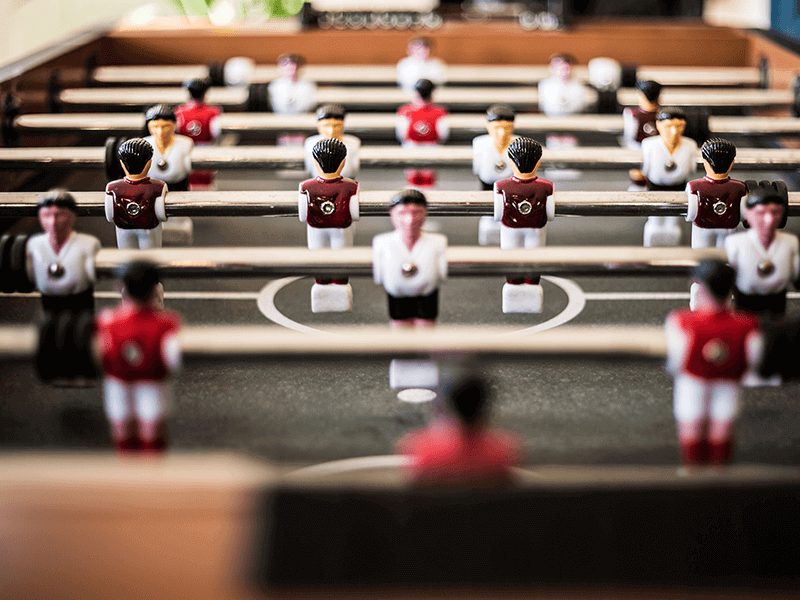 Close-up of a foosball table showing red and white uniformed player figures arranged in rows, with the focus on the central players.