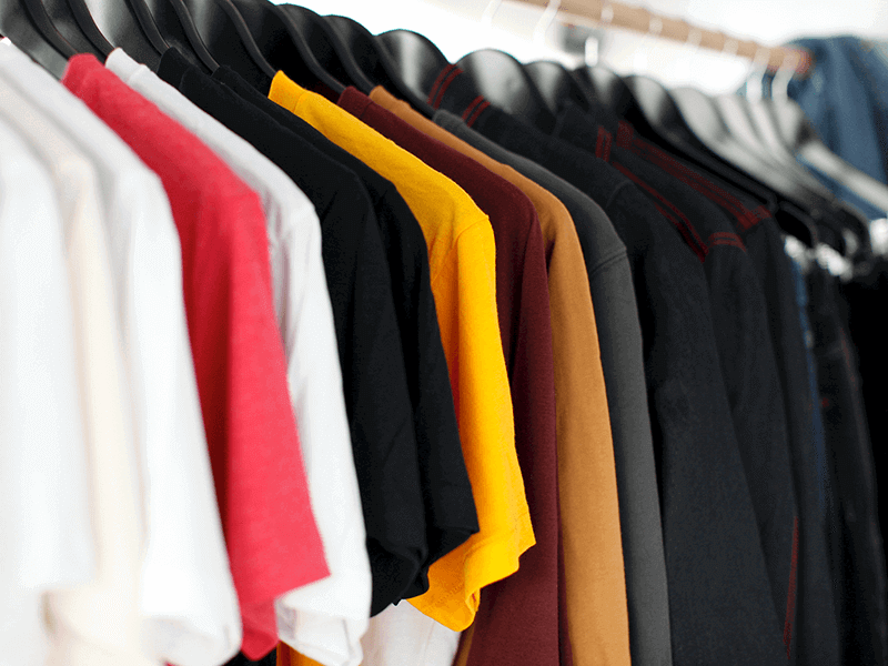 A row of clothes hangers holding various colored t-shirts, including white, red, black, yellow, brown, and grey, on a clothing rack.